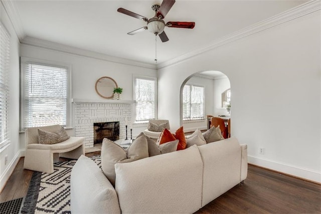 living room with a brick fireplace, baseboards, arched walkways, and wood finished floors