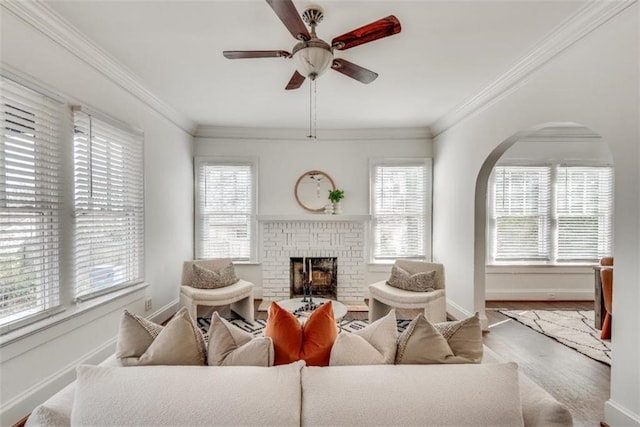 living room with baseboards, ceiling fan, a brick fireplace, and crown molding