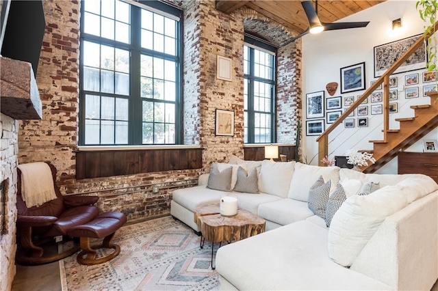 living room featuring brick wall, a high ceiling, stairway, and a ceiling fan