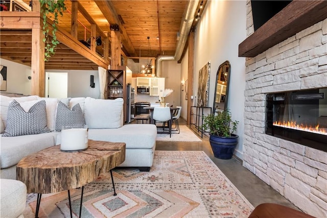 living area with a stone fireplace, concrete floors, a towering ceiling, and wood ceiling