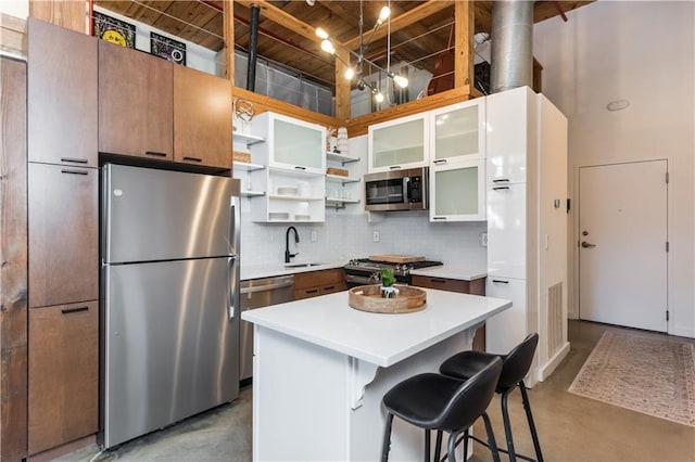 kitchen with open shelves, concrete floors, stainless steel appliances, and a sink