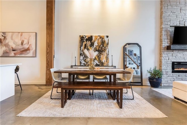 dining area featuring a stone fireplace, finished concrete flooring, and baseboards