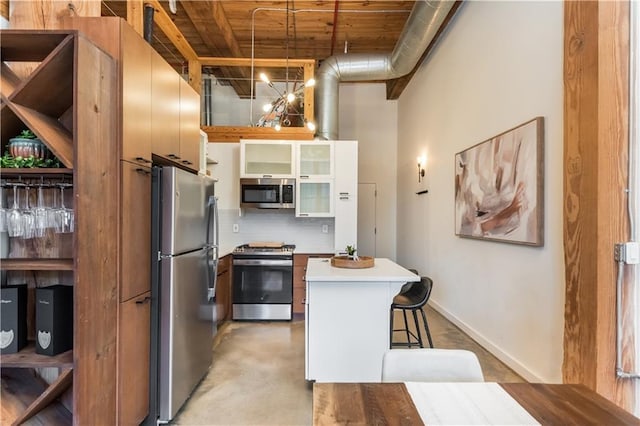 kitchen featuring light countertops, a towering ceiling, appliances with stainless steel finishes, a kitchen island, and a kitchen bar