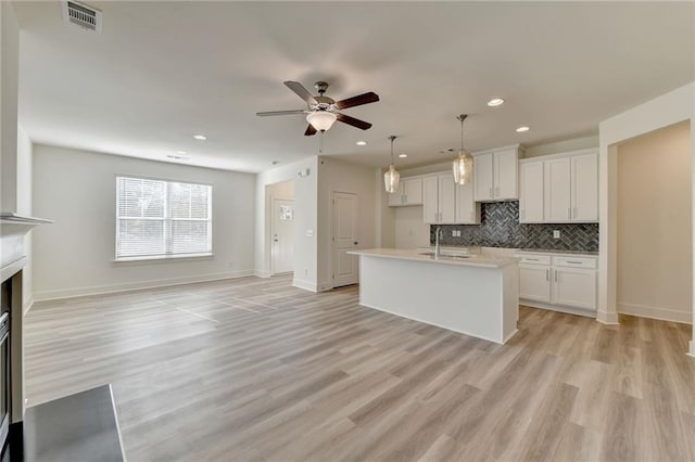 kitchen featuring light wood-type flooring, white cabinetry, hanging light fixtures, and a kitchen island with sink