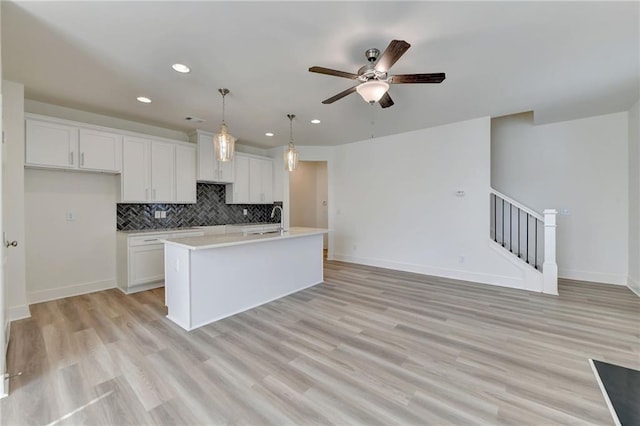 kitchen featuring hanging light fixtures, light hardwood / wood-style floors, white cabinetry, and an island with sink