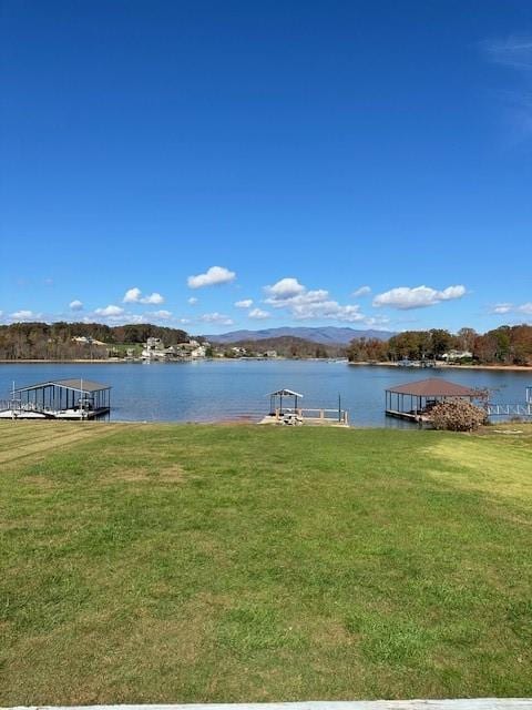 view of dock with a water and mountain view and a lawn