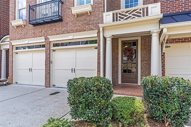 view of exterior entry with a garage, concrete driveway, and brick siding