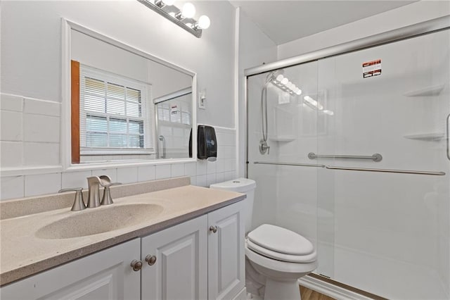 bathroom with vanity, toilet, tile walls, and a shower with shower door