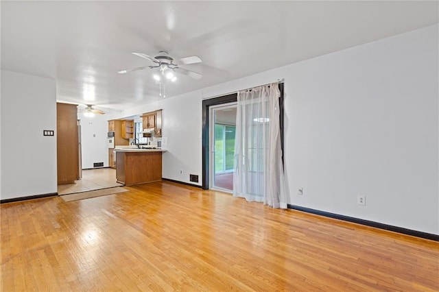 unfurnished living room with ceiling fan, sink, and light hardwood / wood-style floors