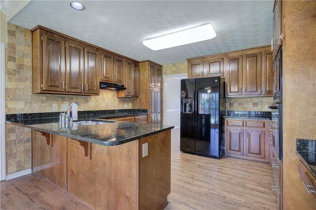 kitchen featuring light wood-type flooring, sink, a breakfast bar, and black appliances