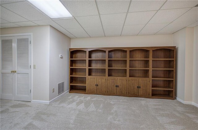 interior space with a paneled ceiling and light carpet