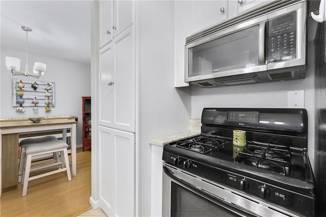 kitchen with gas stove, white cabinetry, decorative light fixtures, light wood-type flooring, and a notable chandelier