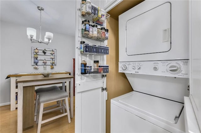 clothes washing area with stacked washer and dryer, light hardwood / wood-style flooring, and a chandelier