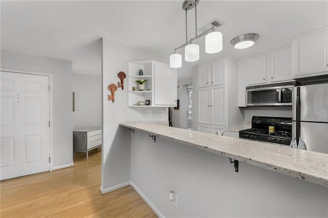 kitchen with decorative light fixtures, white cabinetry, light stone counters, stainless steel appliances, and light hardwood / wood-style flooring