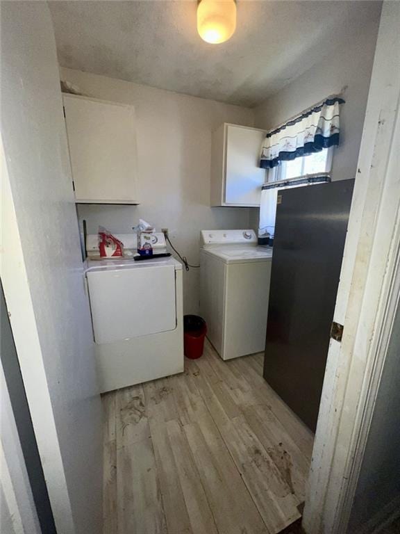 clothes washing area with washer and dryer, cabinet space, and light wood-type flooring