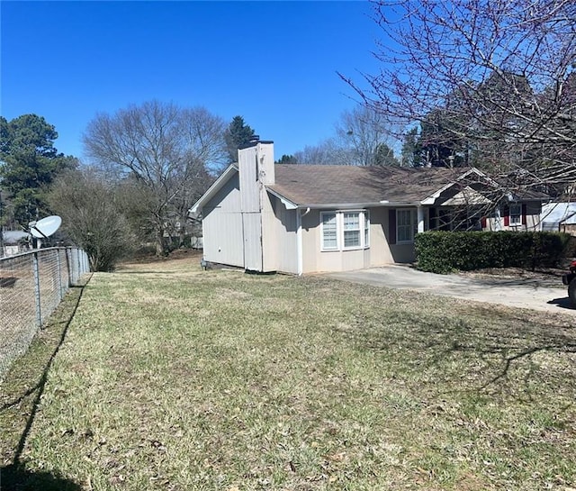 view of side of property with a lawn, a chimney, and fence