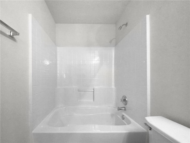 bathroom featuring toilet, a textured ceiling, and tiled shower / bath