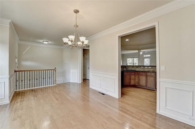 unfurnished dining area featuring crown molding, a notable chandelier, light wood finished floors, visible vents, and a decorative wall