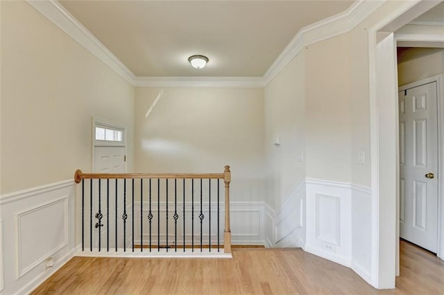 interior space featuring ornamental molding, wainscoting, a decorative wall, and wood finished floors