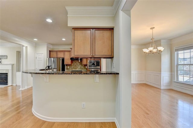 kitchen featuring pendant lighting, brown cabinetry, freestanding refrigerator, dark stone countertops, and a kitchen bar