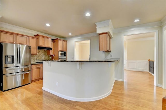 kitchen featuring appliances with stainless steel finishes, dark stone counters, brown cabinetry, and a kitchen breakfast bar