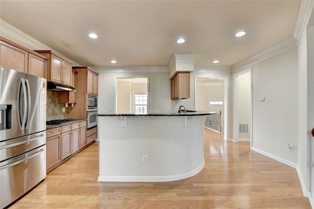 kitchen featuring brown cabinets, under cabinet range hood, appliances with stainless steel finishes, and dark stone counters