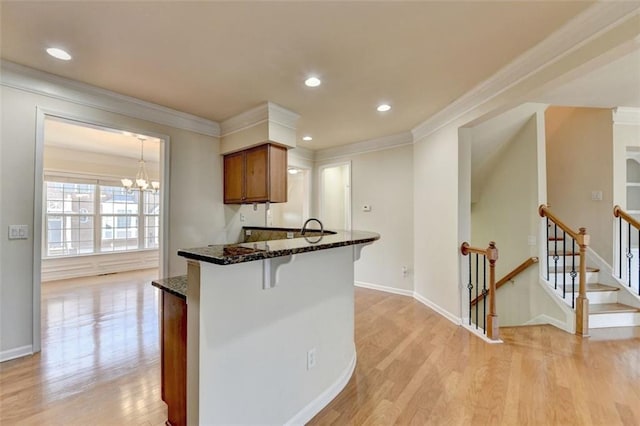 kitchen featuring light wood-style flooring, ornamental molding, brown cabinets, and dark stone countertops