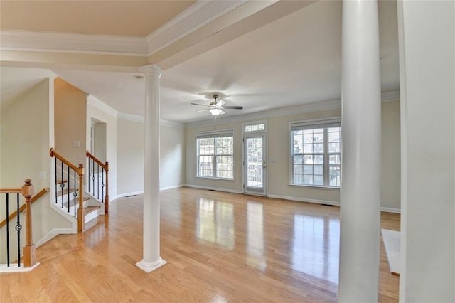 empty room with crown molding, stairway, ceiling fan, light wood-type flooring, and ornate columns