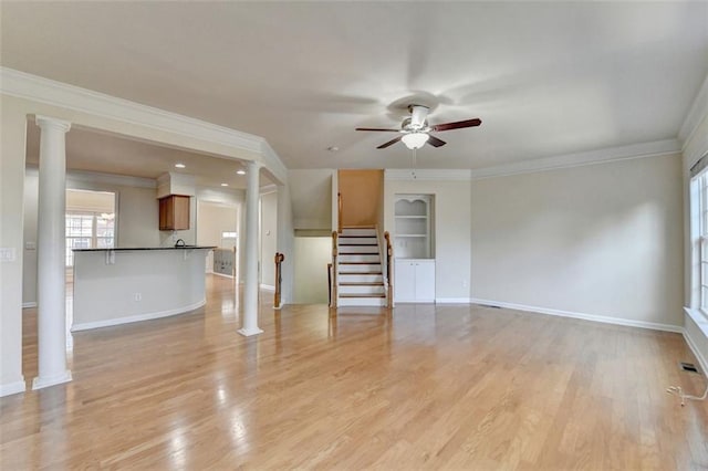 unfurnished living room with decorative columns, stairway, light wood-style floors, ornamental molding, and baseboards