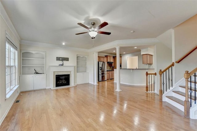 unfurnished living room featuring light wood-style floors, decorative columns, built in features, and a glass covered fireplace