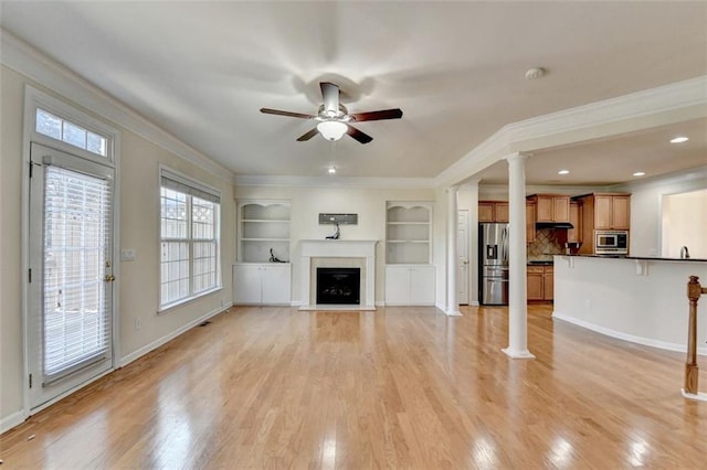 unfurnished living room with a fireplace with raised hearth, a ceiling fan, ornate columns, light wood finished floors, and crown molding