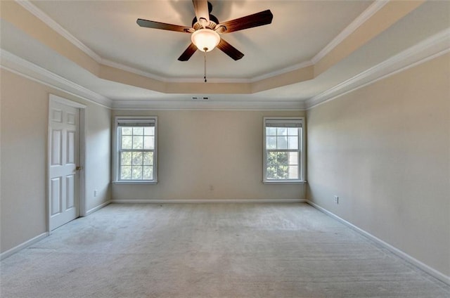 unfurnished room with a tray ceiling, light colored carpet, crown molding, and baseboards