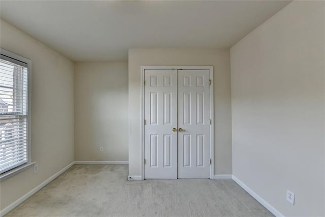 unfurnished bedroom with a closet, light carpet, and baseboards