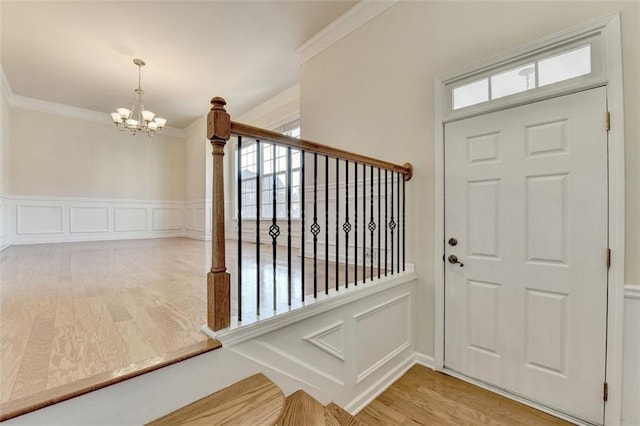 entrance foyer with a chandelier, light wood-style flooring, a decorative wall, stairway, and crown molding