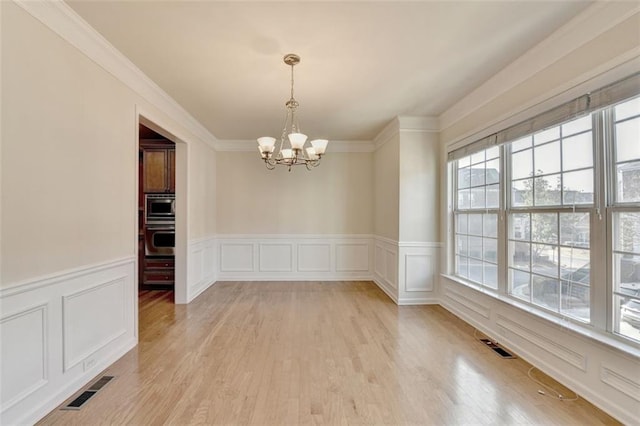 unfurnished dining area featuring a chandelier, light wood finished floors, visible vents, and a decorative wall