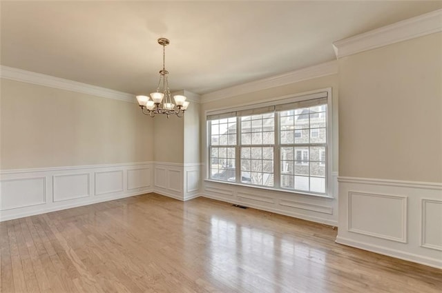 spare room featuring visible vents, wainscoting, light wood-style flooring, ornamental molding, and an inviting chandelier