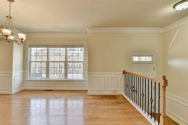 spare room with visible vents, a wainscoted wall, an inviting chandelier, crown molding, and light wood-type flooring