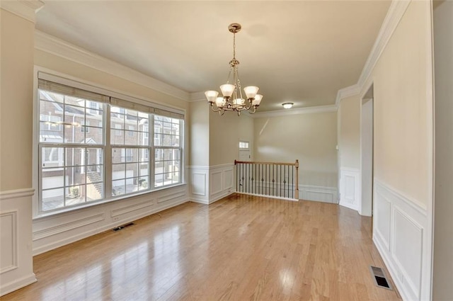 spare room with ornamental molding, light wood-type flooring, visible vents, and a notable chandelier