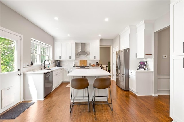 kitchen with white cabinets, wall chimney exhaust hood, a kitchen island, stainless steel appliances, and a sink