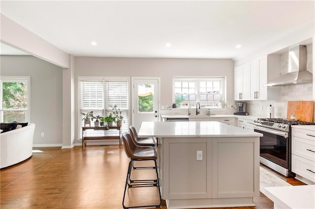 kitchen with a healthy amount of sunlight, wall chimney exhaust hood, a kitchen island, and stainless steel gas range oven