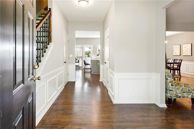 foyer entrance featuring stairway, a decorative wall, dark wood-type flooring, and wainscoting