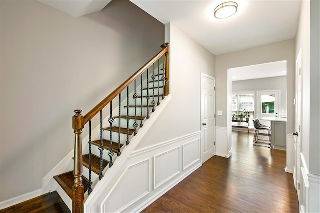 stairs with wainscoting, wood finished floors, and a decorative wall