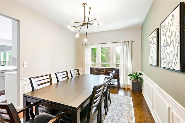 dining space featuring a chandelier, wainscoting, dark wood finished floors, and a decorative wall