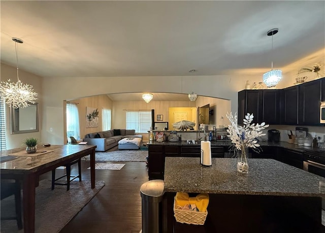 2979 Dungeness Dr, Douglasville, GA 30135 - kitchen featuring dark wood finished floors, dark cabinetry, dark stone countertops, a chandelier, and arched walkways
