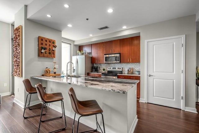 kitchen with appliances with stainless steel finishes, kitchen peninsula, dark hardwood / wood-style floors, tasteful backsplash, and a kitchen breakfast bar