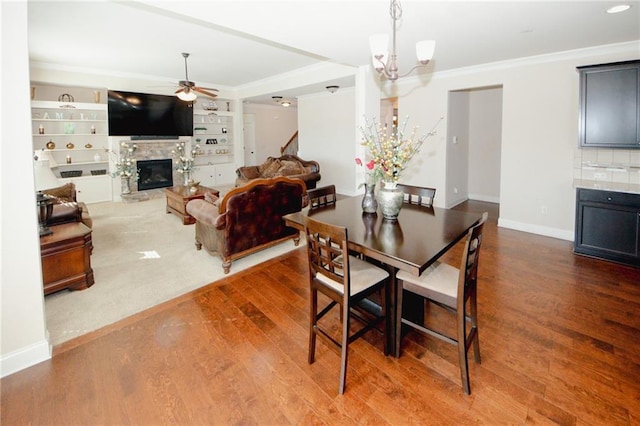 4594 Marching Ln, Fairburn, GA 30213 - dining space featuring baseboards, a glass covered fireplace, wood finished floors, crown molding, and ceiling fan with notable chandelier