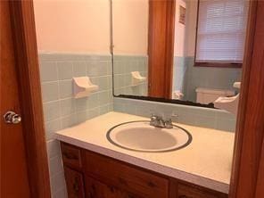 bathroom with toilet, vanity, and tile walls