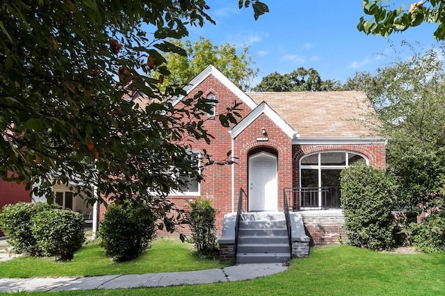 view of front of property with brick siding, a front lawn, and roof with shingles