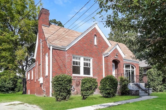 view of front of property featuring a shingled roof, a front yard, a chimney, and brick siding