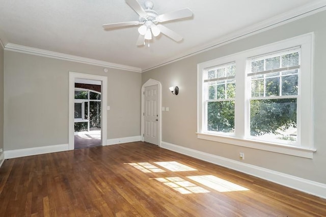 unfurnished room featuring baseboards, arched walkways, a ceiling fan, wood finished floors, and crown molding